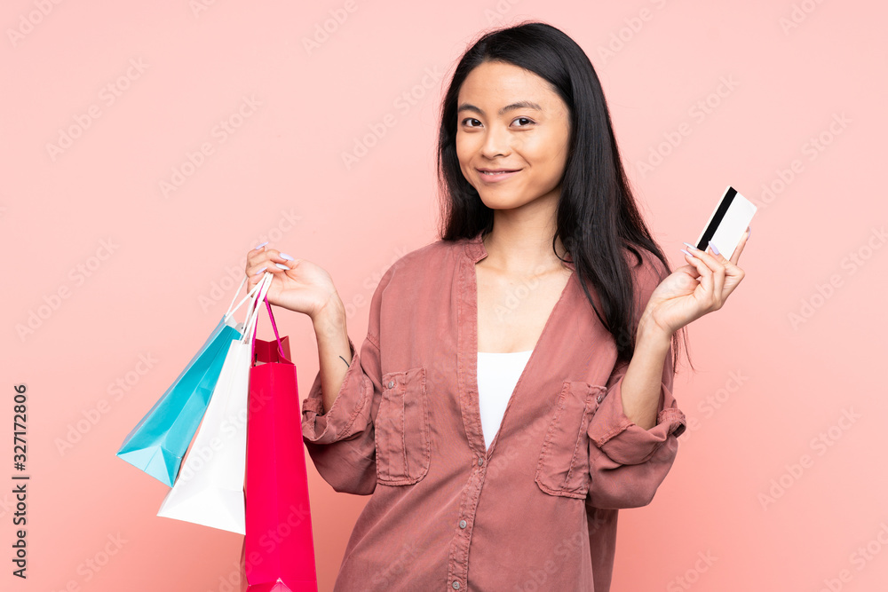 Teenager Chinese girl isolated on pink background holding shopping bags and a credit card Teenager Chinese girl isolated on pink background holding shopping bags and a credit card
