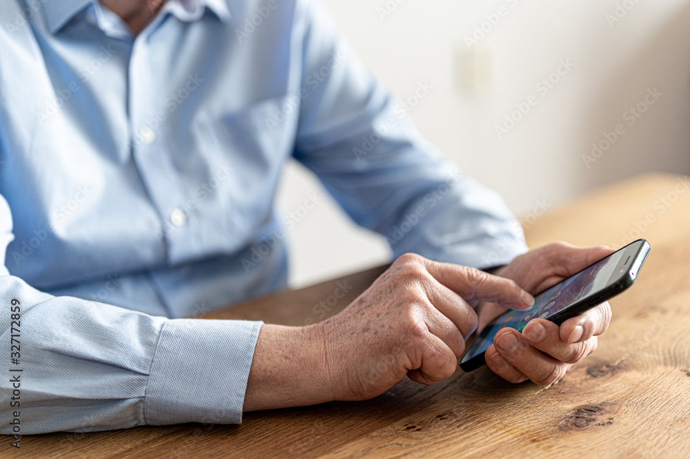 Older businessman working with his smartphone at a wooden table.