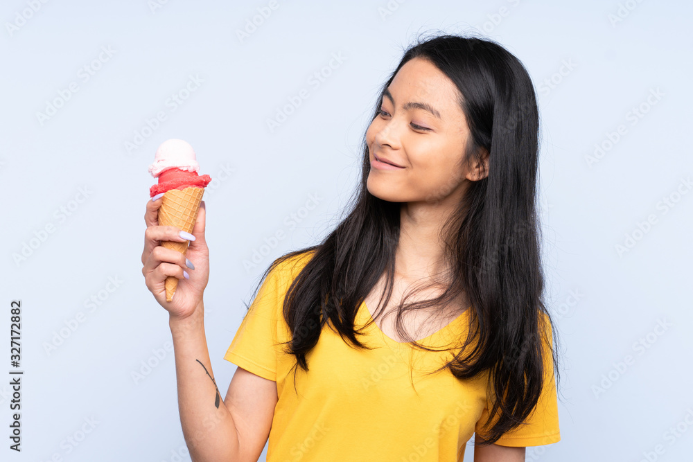 Teenager Asian girl with a cornet ice cream isolated on blue background with happy expression Teenager Asian girl with a cornet ice cream isolated on blue background with happy expression