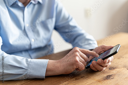 Older businessman working with his smartphone at a wooden table.