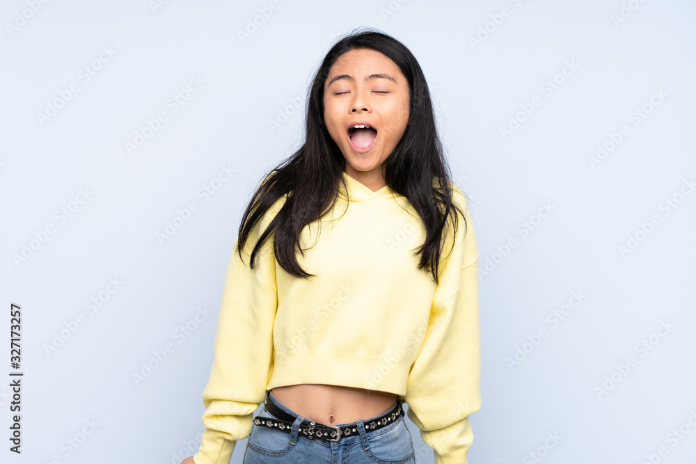 Teenager Chinese woman isolated on blue background shouting to the front with mouth wide open Teenager Chinese woman isolated on blue background shouting to the front with mouth wide open