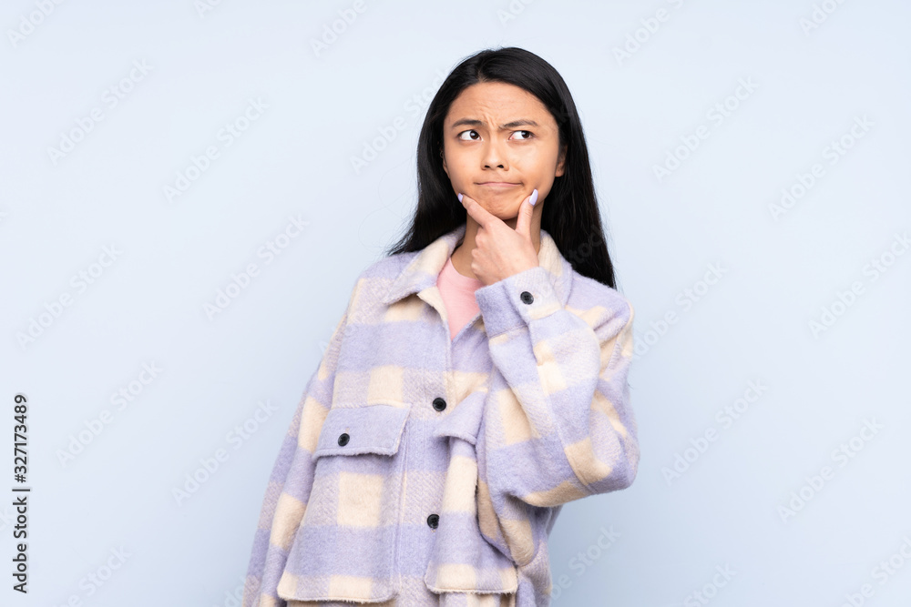Teenager Chinese woman isolated on blue background having doubts Teenager Chinese woman isolated on blue background having doubts