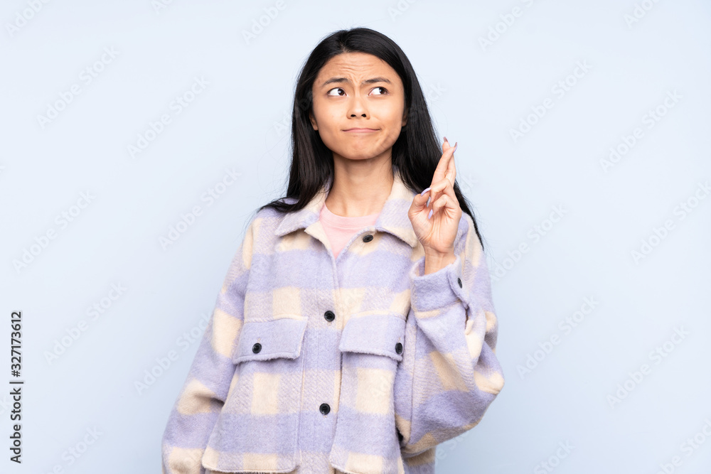 Teenager Chinese woman isolated on blue background with fingers crossing and wishing the best Teenager Chinese woman isolated on blue background with fingers crossing and wishing the best