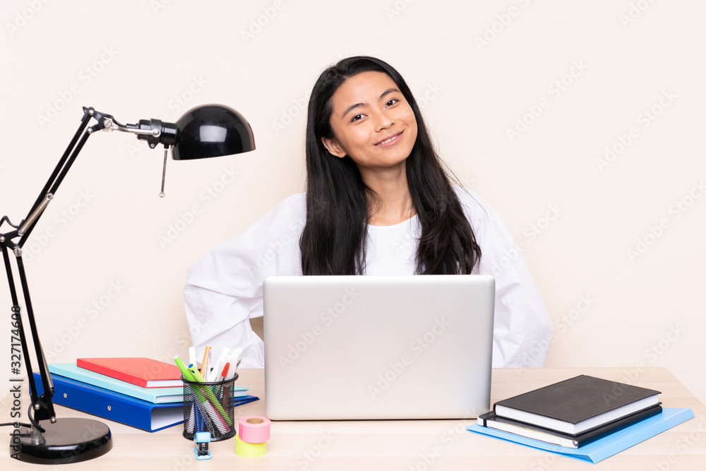 Student asian girl in a workplace with a laptop isolated on beige background posing with arms at hip and smiling Student asian girl in a workplace with a laptop isolated on beige background posing with arms at hip and smiling