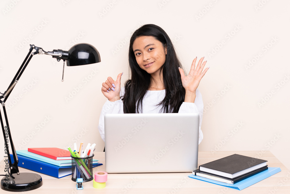 Student asian girl in a workplace with a laptop isolated on beige background counting six with fingers Student asian girl in a workplace with a laptop isolated on beige background counting six with fingers