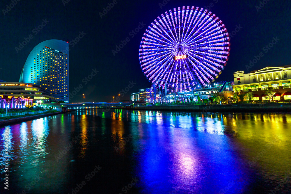 Yokohama Cityscape in Japan of Minato Mirai District at night. Colorful ferris wheel reflected in the bay water.