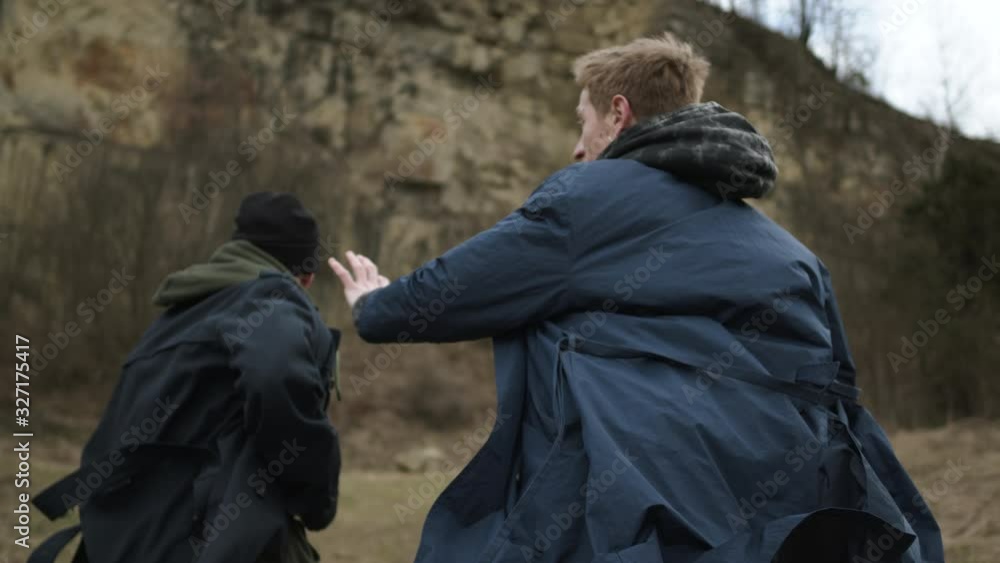 Two Young Guys Running Forward. Guys In Raincoats On Rock Background. View From The Back. Two Young Guys Running Forward. Guys In Raincoats On Rock Background. View From The Back.