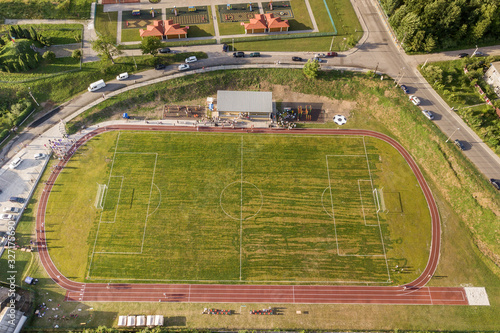 Aerial view of a football field on a stadium covered with green grass in rural town area.