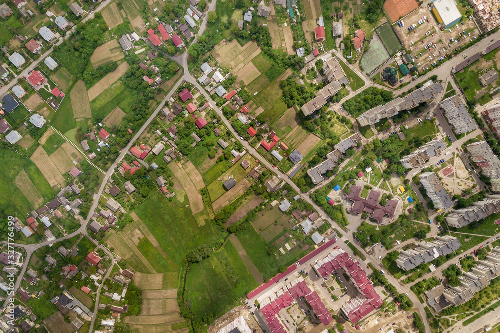 Fototapeta premium Aerial view of town or city with rows of buildings and curvy streets in summer. Urban landscape from above.