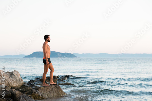 Young man standing on the rock enjoying the sunset by the sea