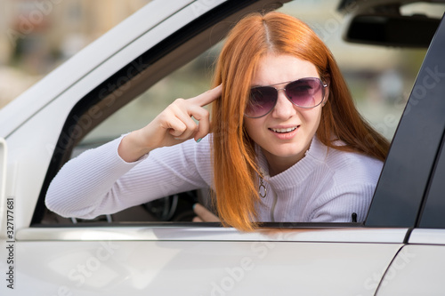 Closeup portrait of pissed off displeased angry aggressive woman driving a car shouting at someone with finger to temple gesture. © bilanol
