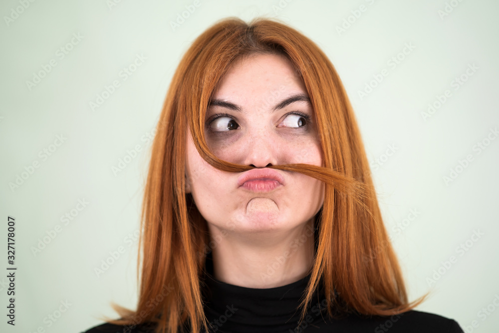 Close up portrait of funny girl holding long red hair like a mustache under her nose. Close up portrait of funny girl holding long red hair like a mustache under her nose.