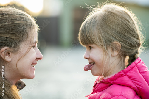 Close up portrait of young mom and her daughter girl making faces to each other outdoors.
