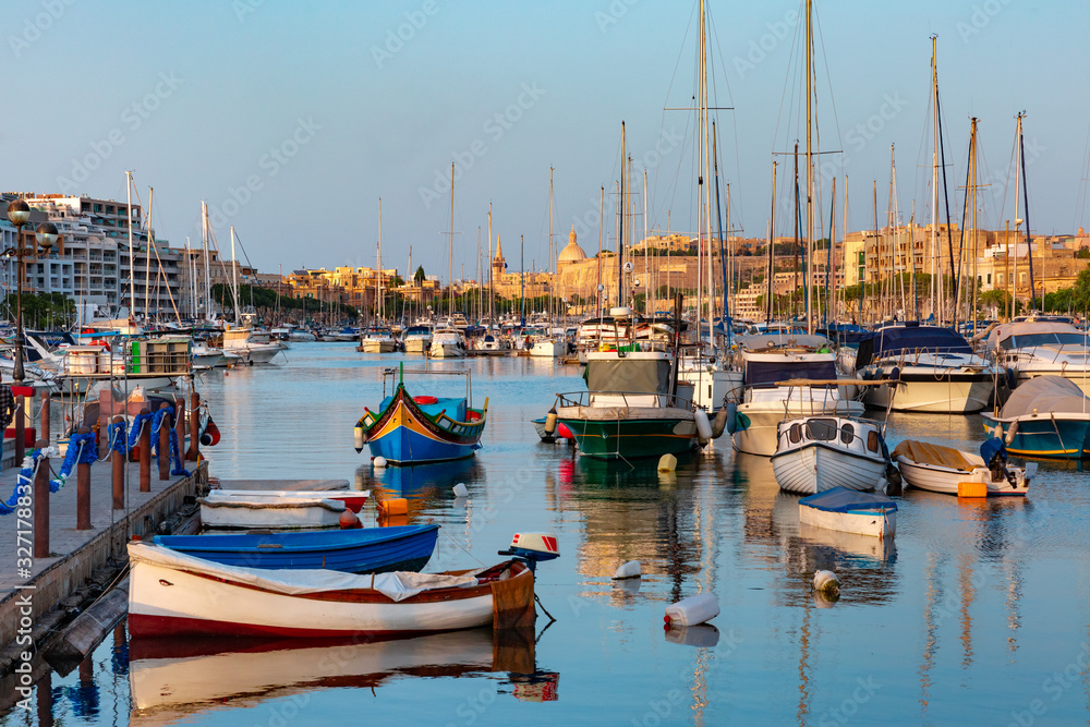 Valletta harbour with yachts and multicolored fishing boats Luzzu with eyes, church and fortress, illuminated by sunset light, Malta