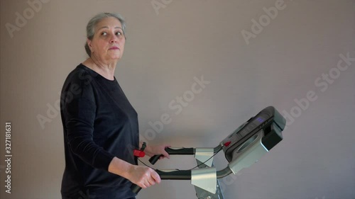 Caucasian senior woman exercising on treadmill. She is change training mode or walk speed.