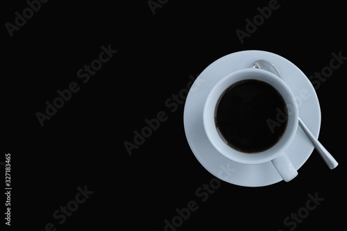 Top view of a white coffee cup with saucers and spoons on the right side of the black background, there is a space for lettering.
