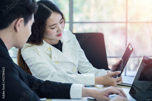 Two young Asian business colleagues using tablet at meeting in modern office. Smart coworkers discuss and brainstorm for new project planning together. Communication and business concept, Daylight. photo