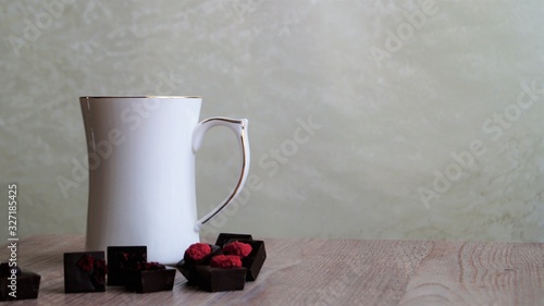 white mug and dark chocolate candies decorated with dried fruits on a wooden table on a light background photo