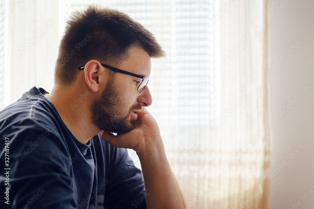 Young caucasian man adult wearing eyeglasses sitting by the table short hair and beard working on computer laptop at home browsing internet thinking side view Young caucasian man adult wearing eyeglasses sitting by the table short hair and beard working on computer laptop at home browsing internet thinking side view