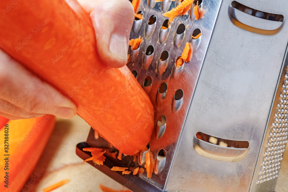 Grating fresh juicy carrot on stainless steel grater close-up