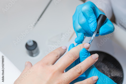 Manicurist paints client s nails with a transparent nail polish.