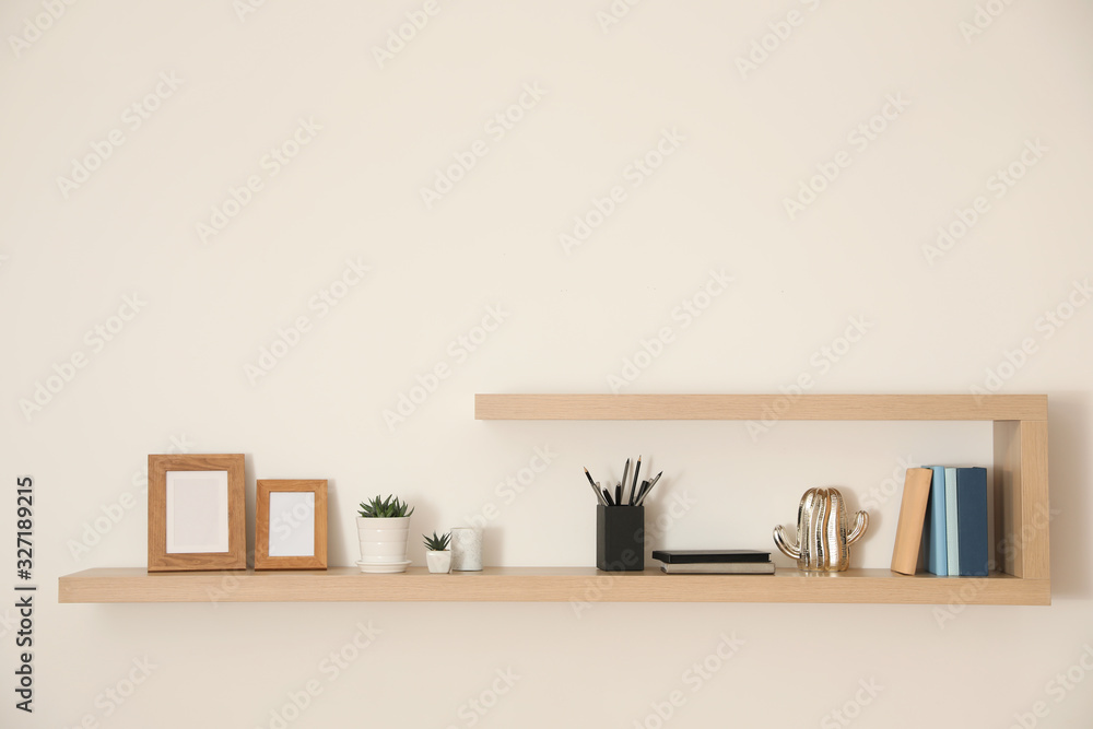 Wooden shelves with books, photo frames and decorative elements on light wall Wooden shelves with books, photo frames and decorative elements on light wall