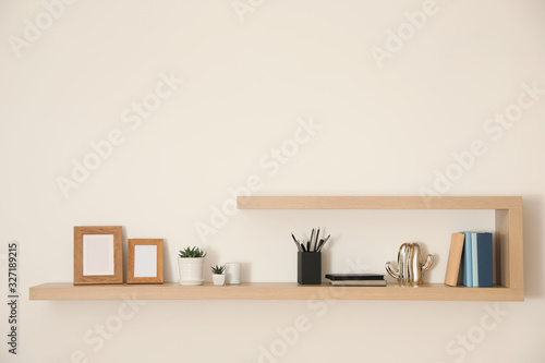 Wooden shelves with books, photo frames and decorative elements on light wall