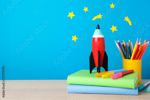 Bright toy rocket and school supplies on wooden desk. Space for text