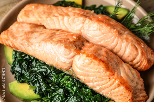 Tasty salmon with spinach and avocado on plate, closeup
