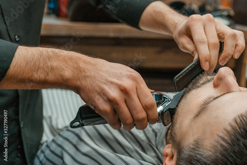 Beauty shop for men. Shaving a beard in a barbershop. Barber cuts his beard with a razor and clipper. close up Brutal haircuts. Hairdresser equipment. Selective focus.