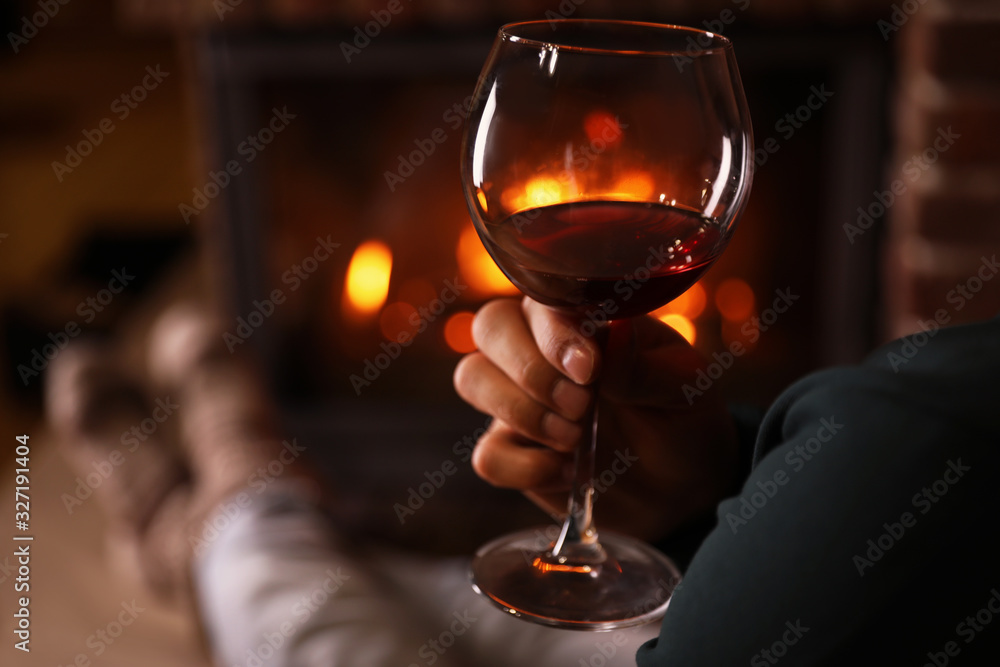 Man with glass of wine near fireplace at home, closeup
