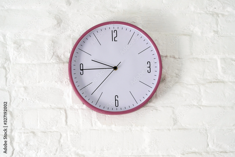Round clock with arrows and numbers on a white brick wall. Clock on the ...