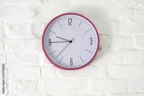 Round clock with arrows and numbers on a white brick wall. Clock on the wall
