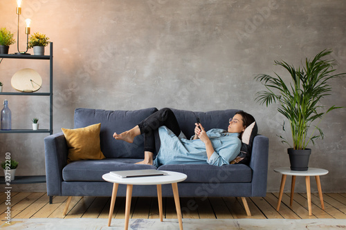 Young woman with Glasses is Lying on the Couch and Texting on the Phone.