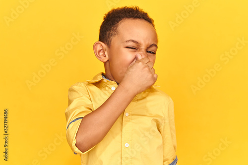 Photos Isolated shot of emotional disgusted African boy smelling something stinky and disgusting, pinching nose