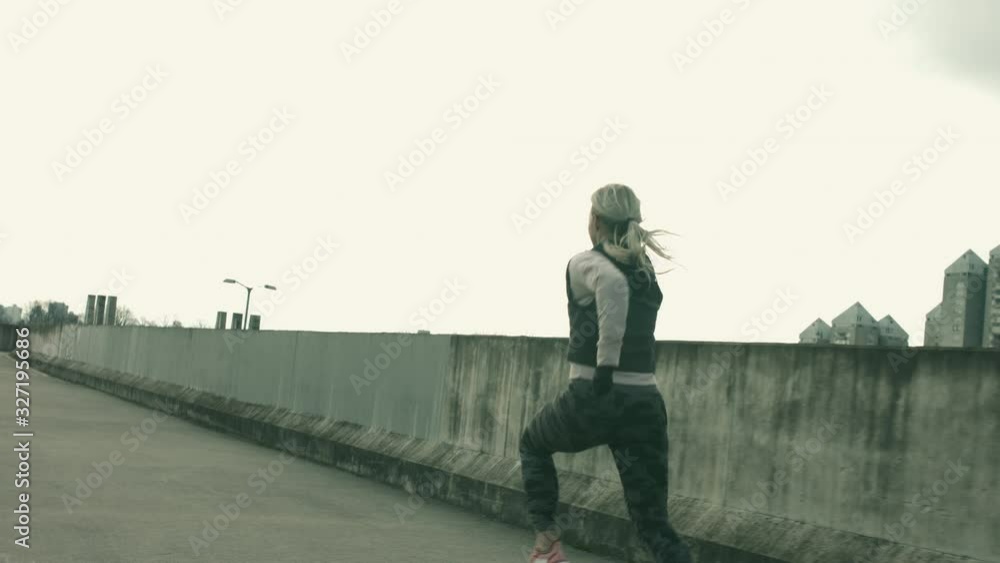 Beautiful athletic woman running in urban area. Shot in slow motion with concrete fence and tall buildings in background. Beautiful athletic woman running in urban area. Shot in slow motion with concrete fence and tall buildings in background.