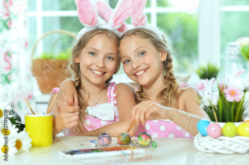 Sisters wearing rabbit ears decorating Easter eggs at home
