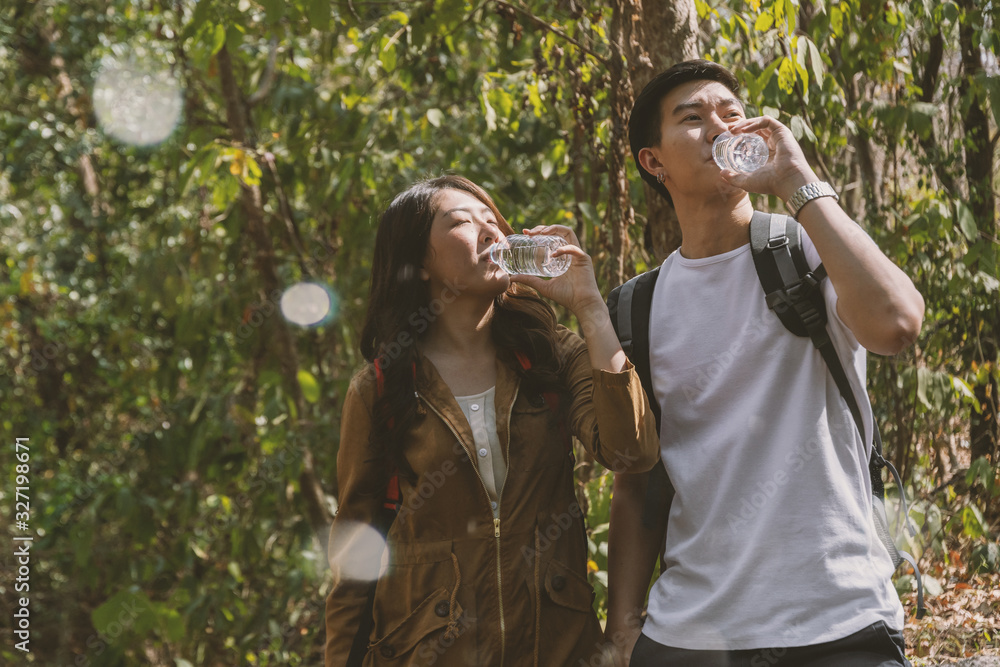 Naklejka premium Asian young couple hiking in the forest have a break and drinking water. Travel and adventure concept.