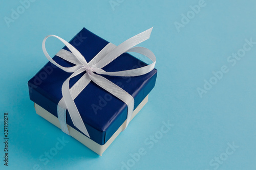 Gift box with a white ribbon and a bow on a blue background. Selective focus.