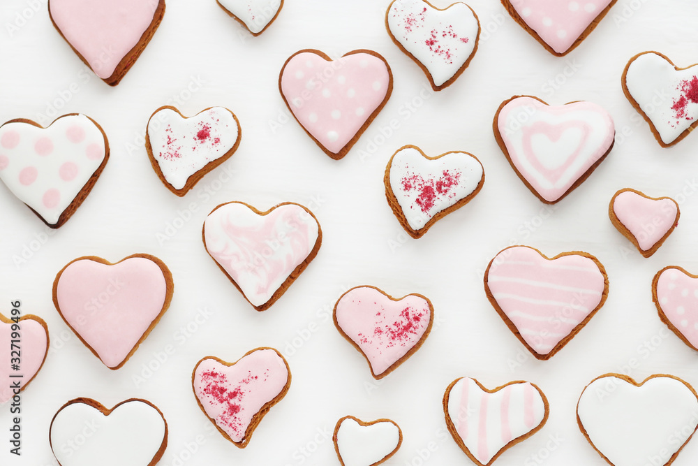 pattern of gingerbread cookies in the shape of a heart decorated with white and pink glaze on a white wooden background..