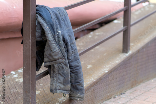 Fotografía old dirty jacket hanging on the railing. Homeless, poverty, need.