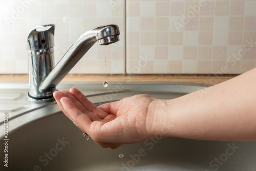 A drop of water drips from faucet in human palm above round metal kitchen sink
