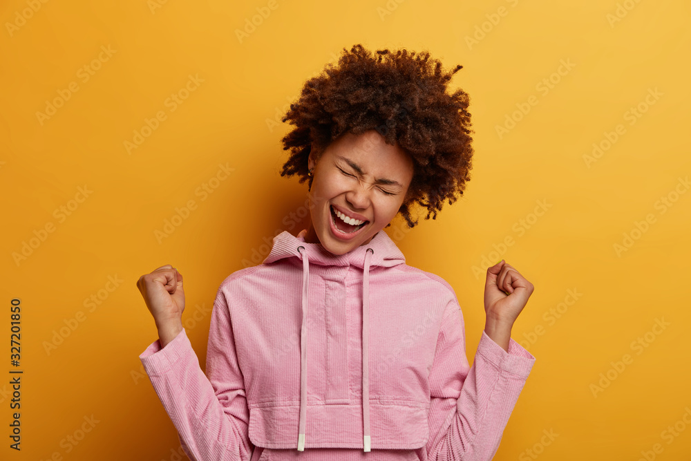 Lucky excited pretty woman clenches fists, shouts hooray, celebrates good news, tilts head, dressed casually, wears pink hoodie, enjoys sweet success, feels taste of victory, wears velvet sweatshirt Lucky excited pretty woman clenches fists, shouts hooray, celebrates good news, tilts head, dressed casually, wears pink hoodie, enjoys sweet success, feels taste of victory, wears velvet sweatshirt