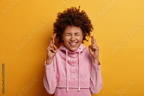 Photography Pleased curly woman crosses fingers, wishes fortune before exam, has great hope