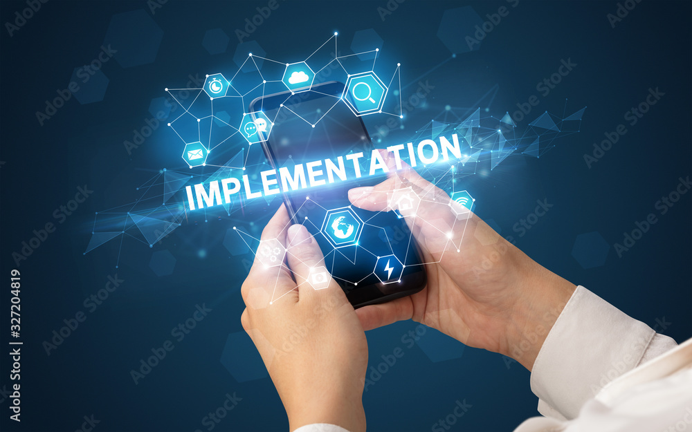 Female hand holding smartphone with IMPLEMENTATION inscription, modern technology concept Female hand holding smartphone with IMPLEMENTATION inscription, modern technology concept