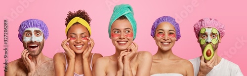 Three mixed race women apply gel patches under eyes to reduce wrinkles, express positive emotions, two men wear clay masks with cucumber slices, bath caps. Set of five people get beauty treatments