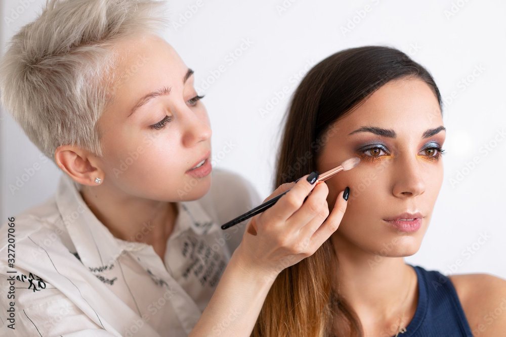 Make-up artist applying bright base color eyeshadow on model's eye and holding a shell with eyeshadow on background Make-up artist applying bright base color eyeshadow on model's eye and holding a shell with eyeshadow on background