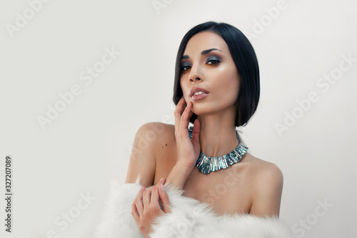 Portrait of a beautiful young Caucasian girl with bare shoulders and beautiful evening make-up dressed in artificial white fur