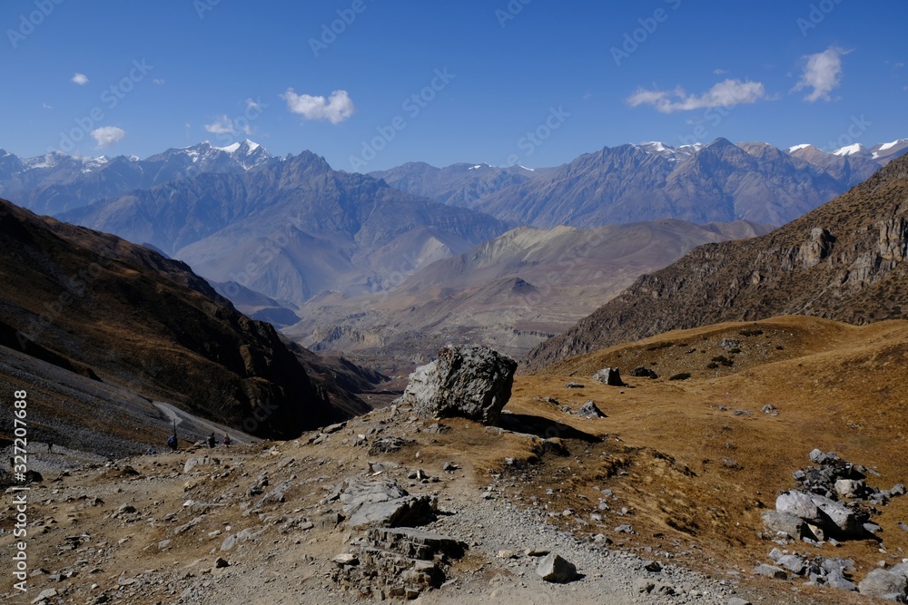Mountain views with a boulder in the foreground on the trail from the Thorong La Pass to Muktinath in Mustang Land, Himalayas, Nepal. During trekking around Annapurna, Annapurna Ciruit Mountain views with a boulder in the foreground on the trail from the Thorong La Pass to Muktinath in Mustang Land, Himalayas, Nepal. During trekking around Annapurna, Annapurna Ciruit