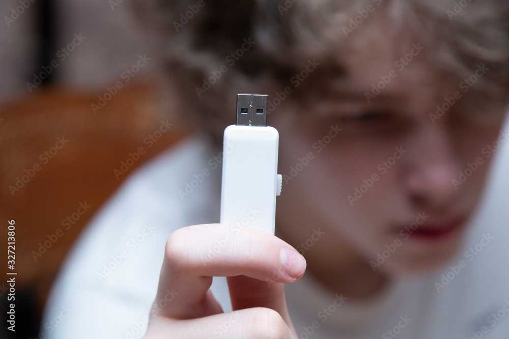White flash drive in the hands of a teenager. - obrazy, fototapety, plakaty 